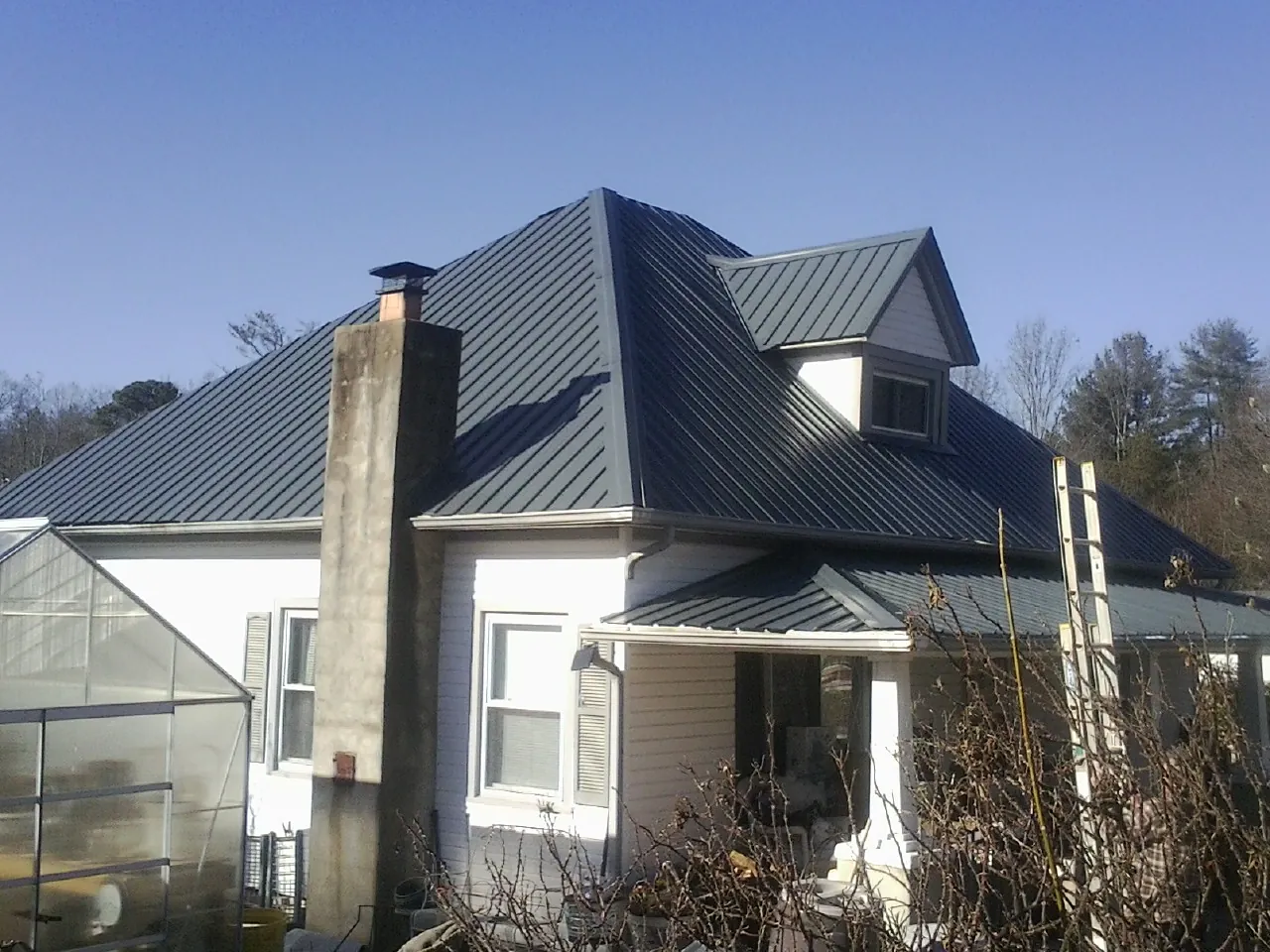 Dark blue standing seam metal roof on a white farmhouse with dormer — Slate & Tile Roof Repair by Roofing Brothers in Idanha
