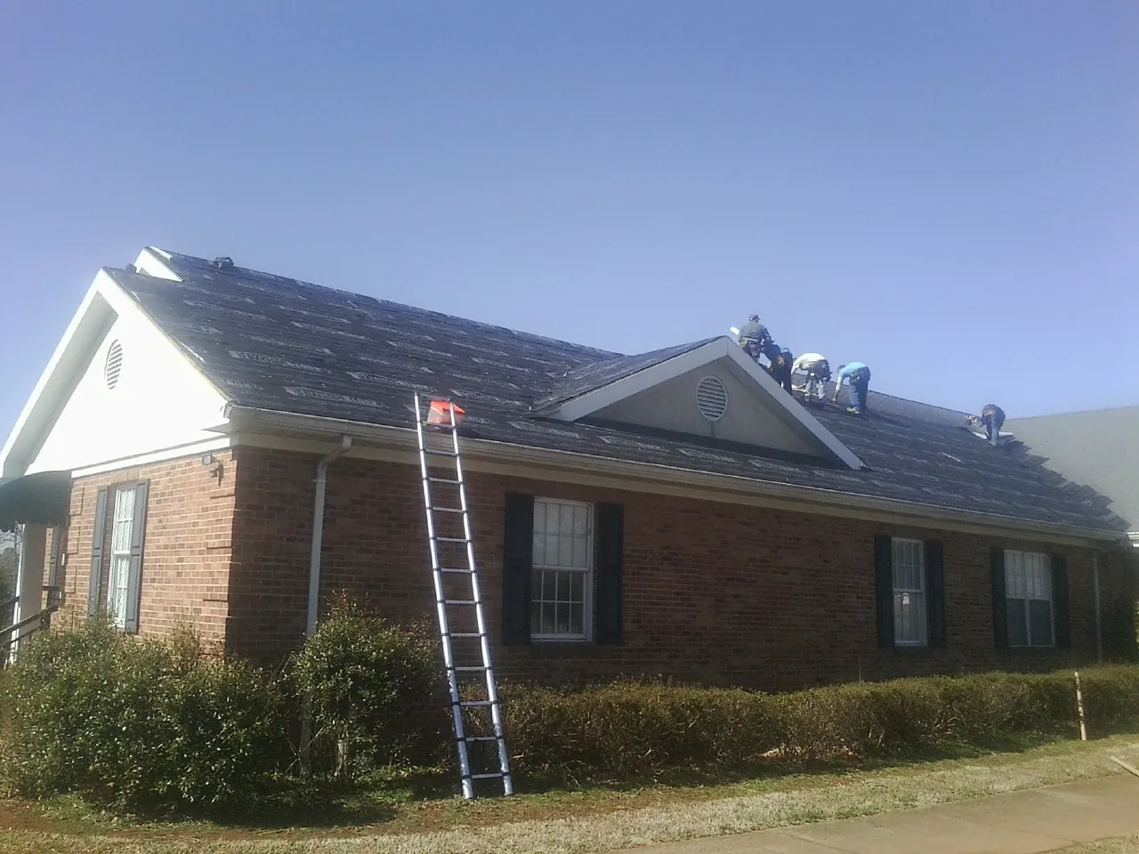 Crew tearing shingles off a brick ranch roof with a ladder set — Emergency Roof Repair work by our crew in Idanha