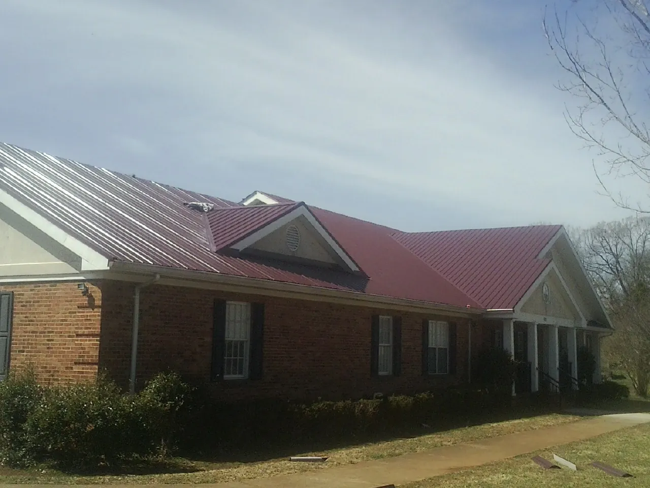 Red metal roof with gabled entries on a long brick building, from a Hail Damage Roof Repair job in Idanha