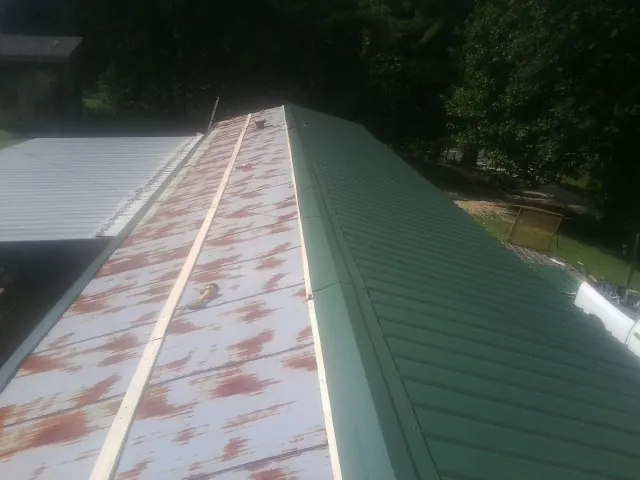 Old rusted panels beside newly installed green metal roofing — Wind Damage Roof Repair by Roofing Brothers in Idanha