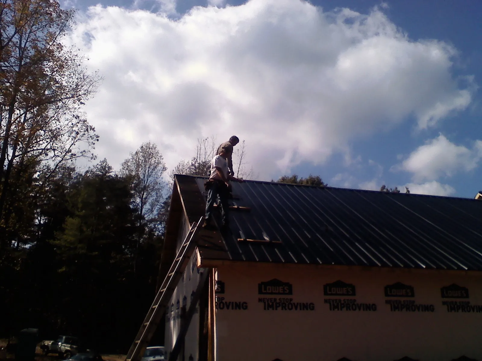 Roofer fastening dark metal panels high against a cloudy sky, from a Roof Inspection job in Idanha