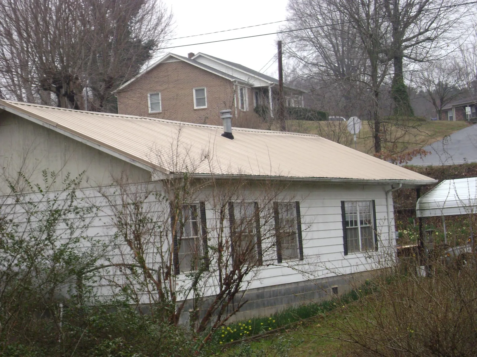 Tan metal roof on a white sided house set into a hillside — Commercial Roofing by Roofing Brothers in Idanha